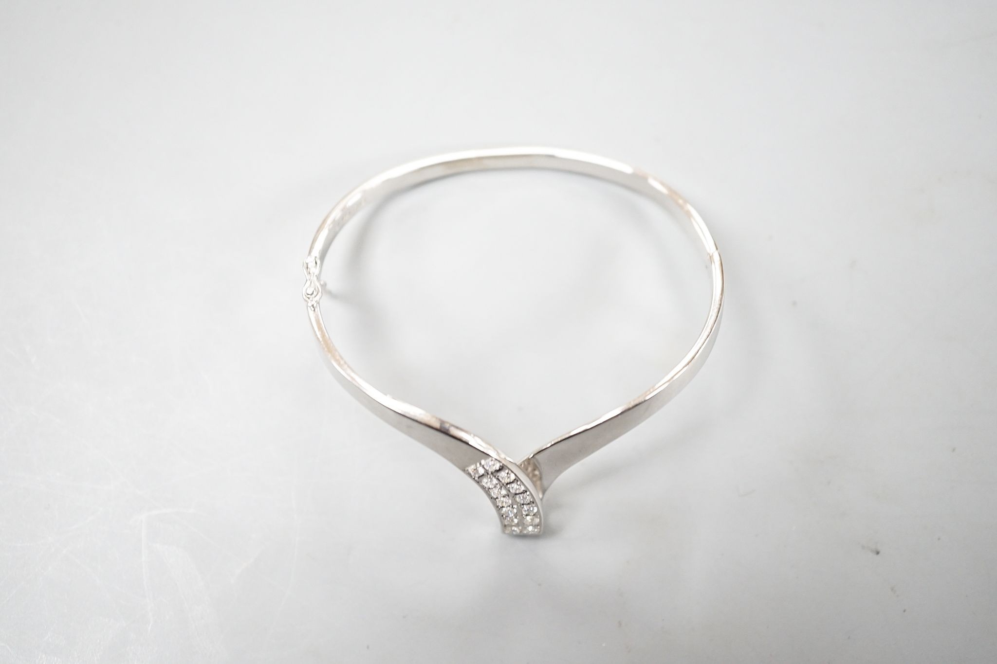 A modern 585 white metal and twelve stone diamond set wishbone shaped hinged bangle, gross 19.7 grams.